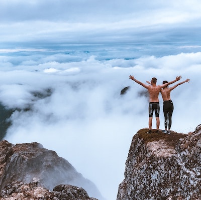 Mut - Mann und Frau stehen auf hohem Felsen und blicken in ein Wolkenmeer und spüren die Freiheit und den Mut das Ziel erreicht zu haben